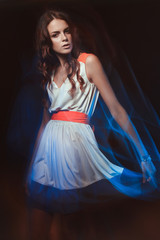 Blurred color art portrait of a girl on a dark background. Fashion woman with beautiful makeup and a light summer dress. Sensual tender image of a girl in motion. Studio portrait