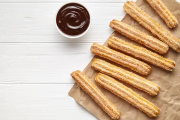 Foto op Plexiglas Churros traditional Spain street fast food baked sweet dough snack with chocolate, rustic decorative paper, white table background. Flat lay top view © GreenArt Photography