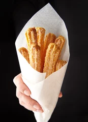 Foto auf Leinwand Churros traditional Spain or Mexican street fast food baked sweet dough snack in hand cone of parchment paper © GreenArt Photography