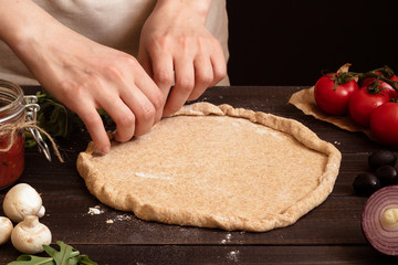 Hands preparing dough for pizza. Pizza ingredients on the wooden table