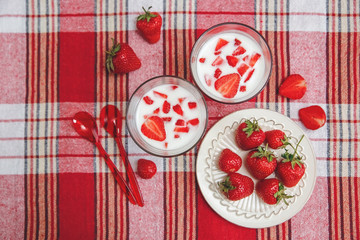 Two Glasses of Yoghurt,Red Fresh Strawberries are in the Ceramic Plate with Plastic Spoons on the Check Tablecloth.Breakfast Organic Healthy Tasty Food.Cooking Vitamins Ingredients.Summer Fruits.