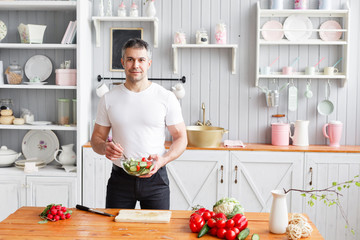 Middle-aged athlete, holding a bowl of a plate with a prepared salad of cucumber and tomato. Vegetarian food