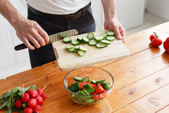 Middle-aged athlete, cuts vegetables salad of cucumber and tomato. Vegetarian food