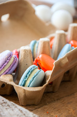 Mix of colorful macarons in a craft paper egg container on a wooden background