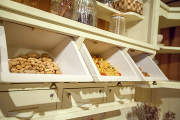 We can see different items of food in separate drawers in a cupboard. There are some hazelnuts and pasta.