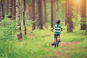 child on a bicycle in the forest in early morning. Boy cycling outdoors in helmet
