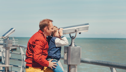 Father helps his little son to look in sea binoculars
