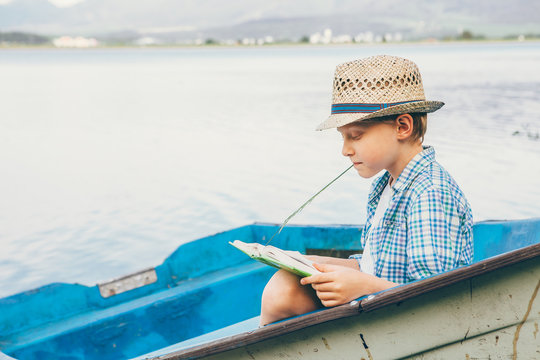 Boy reads a book in old boat on the lake bank