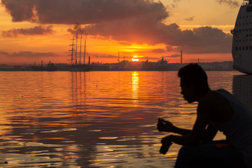 Fototapeta na wymiar Silhouette of man fishing by hand and sail boat at sunrise in Havana port, Cuba