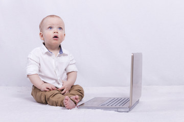 An infant boy in a shirt with laptop. Kid looiking up