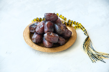 Dried date fruits or kurma served on a old vintage tray with ornaments and beads on a white stone background, ramadan food concept.