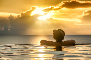 Young woman relaxing on the swimming pool, near the sea in the sunset