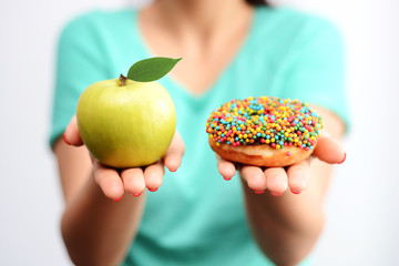 It’s hard to choose healthy food concept, with woman hand holding an green apple and a calorie bomb donut