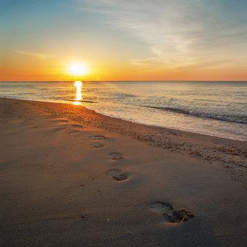 Dawn at the sea, footprints walking along the beach
