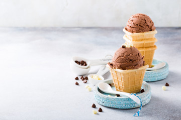 Homemade chocolate ice cream in waffle cups on blue plates on gray stone background. Healthy summer food concept with copy space.