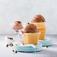 Waffle cups with chocolate ice cream, milk and white chocolate granules in measuring spoons on gray stone background. Healthy summer food concept with copy space.