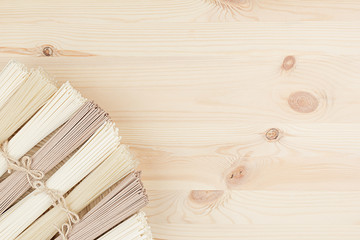 Assortment bundles of raw asian noodles on beige wooden dish on wood board, top view. Decorative border with copy space.