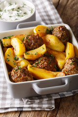 Meat balls with potato wedges in a baking dish and sour cream close-up. Vertical