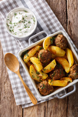 Meat balls with potato wedges in a baking dish and sour cream close-up. vertical top view