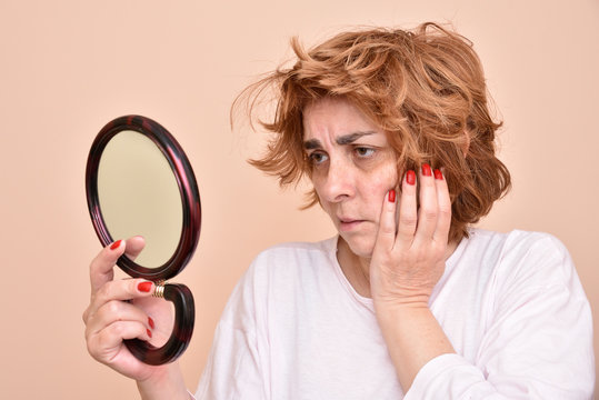 Unhappy And Dissatisfied Middle Aged Woman Looking At Her Skin And Unkempt Hair In The Mirror