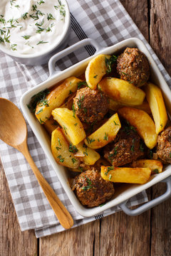 Meat balls with potatoes in a baking dish and sour cream close-up on a table. vertical top view