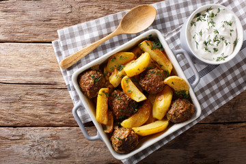 Baked meat balls with potato wedges and sour cream sauce close-up on the table. Horizontal top view