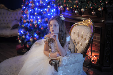 Girl in white dress in the fireplace on background glowing Christmas tree.