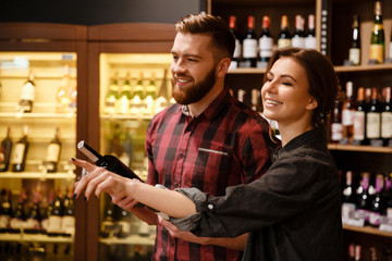 Concentrated happy loving couple in supermarket choosing alcohol.