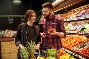 Cheerful loving couple in supermarket choosing fruits.