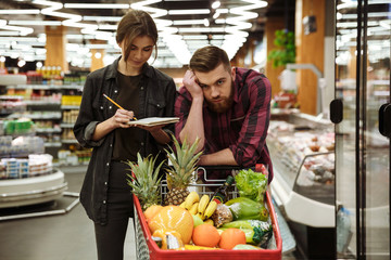 Loving couple in supermarket. Tired man looking at camera.