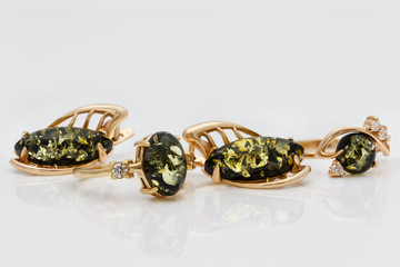 Closeup jewelry set of golden  earrings and rings with authentic natural baltic green amber  on acrylic surface on white  background.