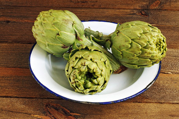 Obraz premium Artichokes, plate and wood background