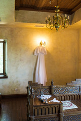 Beautiful white rustic wedding dress hanging on the chandelier in the room