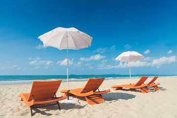 Orange beach chairs and parasols on sandy beach with cloudy blue sky and sea
