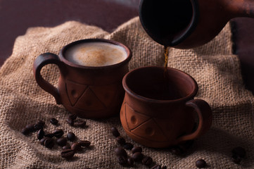 Coffee, morning, coffee beans concept - coffe in earthenware cup and coffe beans on brown background