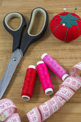 Sewing tools with red pincushion are on the wooden background