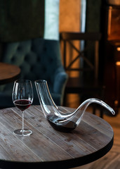 Decanter with red wine and glass on wooden table in interior. Free space for text. Still life