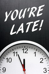 The words You're Late in white text on a blackboard above a wall clock as a reminder of the importance of being on time