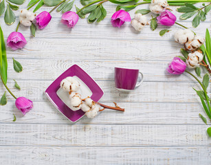 Floral frame with tulips and cotton flower over wood and a porcelain cup and plate in the middle