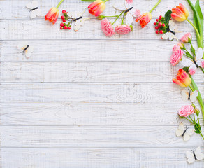 Floral frame with spring flowers and butterflies over wooden background