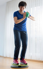 Gleichgewichtstraining auf Wackelbrett in der Physiotherapie Praxis Frau mit Ball