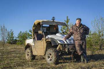 Fototapeta na wymiar Male fisherman, hunter camouflage in a suit standing next to the ATV, SUV in forest, field, summer, men's Hobbies.