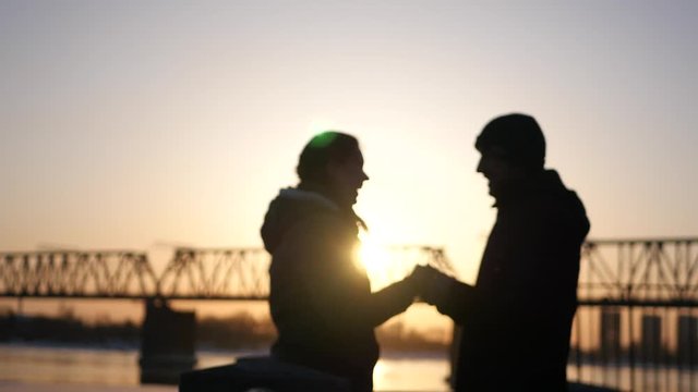 Young happy couple holding each other's hands, smiling against the beautiful sunset and railway bridge. 4k