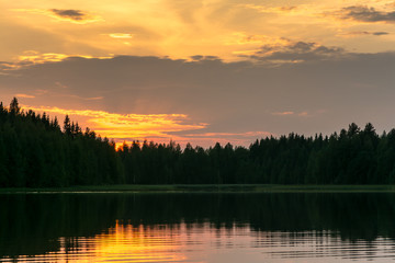 Fototapeta na wymiar Panoramic view on bright sunset at forest lake Savenkaita, Finland