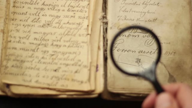 Hands searching in a vintage manuscript with magnifying glass.
