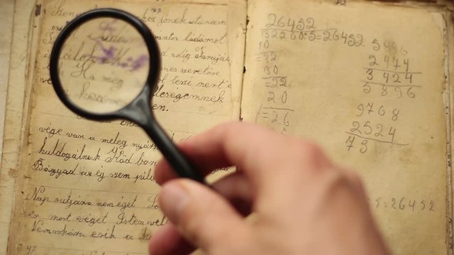 Hands searching in a vintage manuscript with magnifying glass.