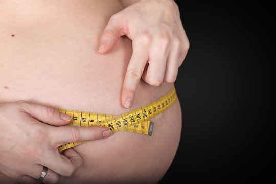 Schwangere beim Messen vom Bauchumfang mit einem gelben Zentimetermaß