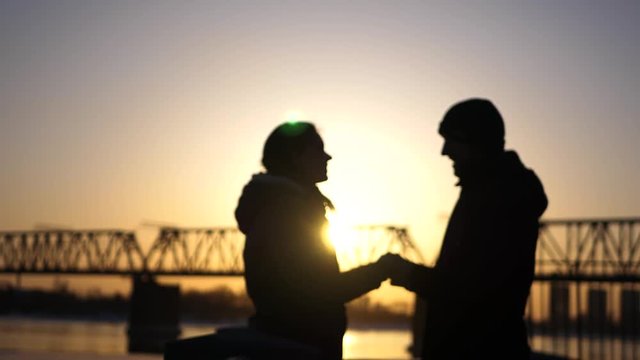 A loving couple, happy man and woman are kissing on the background of a railway bridge and sunset. 4k