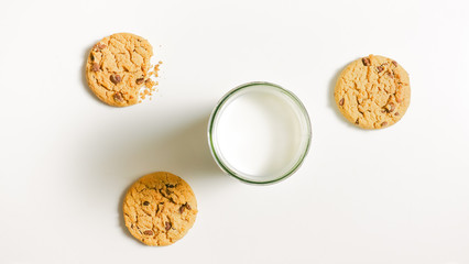 Three round friable cookies and a full glass of milk on the table. One cookies is bitten