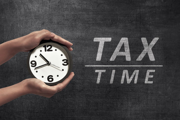 People hand holding black alarm clock beside Tax time announcement